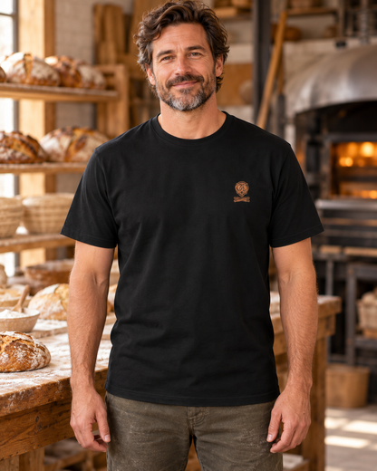Erwachsener Mann trägt das schwarze Workaholicz Bäcker T-Shirt mit kleinem Brustwappen in einer Backstube