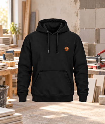 Schwarzer Workaholicz Fliesenleger Hoodie mit kleinem Brustwappen vor Fliesenlegerwerkstatt