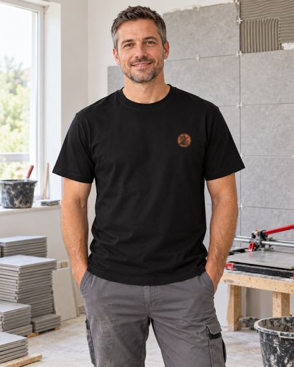 Erwachsener Fliesenleger trägt das schwarze Workaholicz T-Shirt mit kleinem Brustwappen in einem Raum mit Fliesenarbeiten