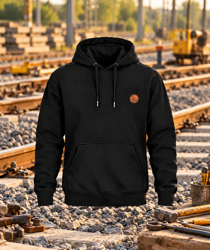 Schwarzer Gleisbauer Hoodie mit kleinem Brustwappen vor einer Gleisbaukulisse