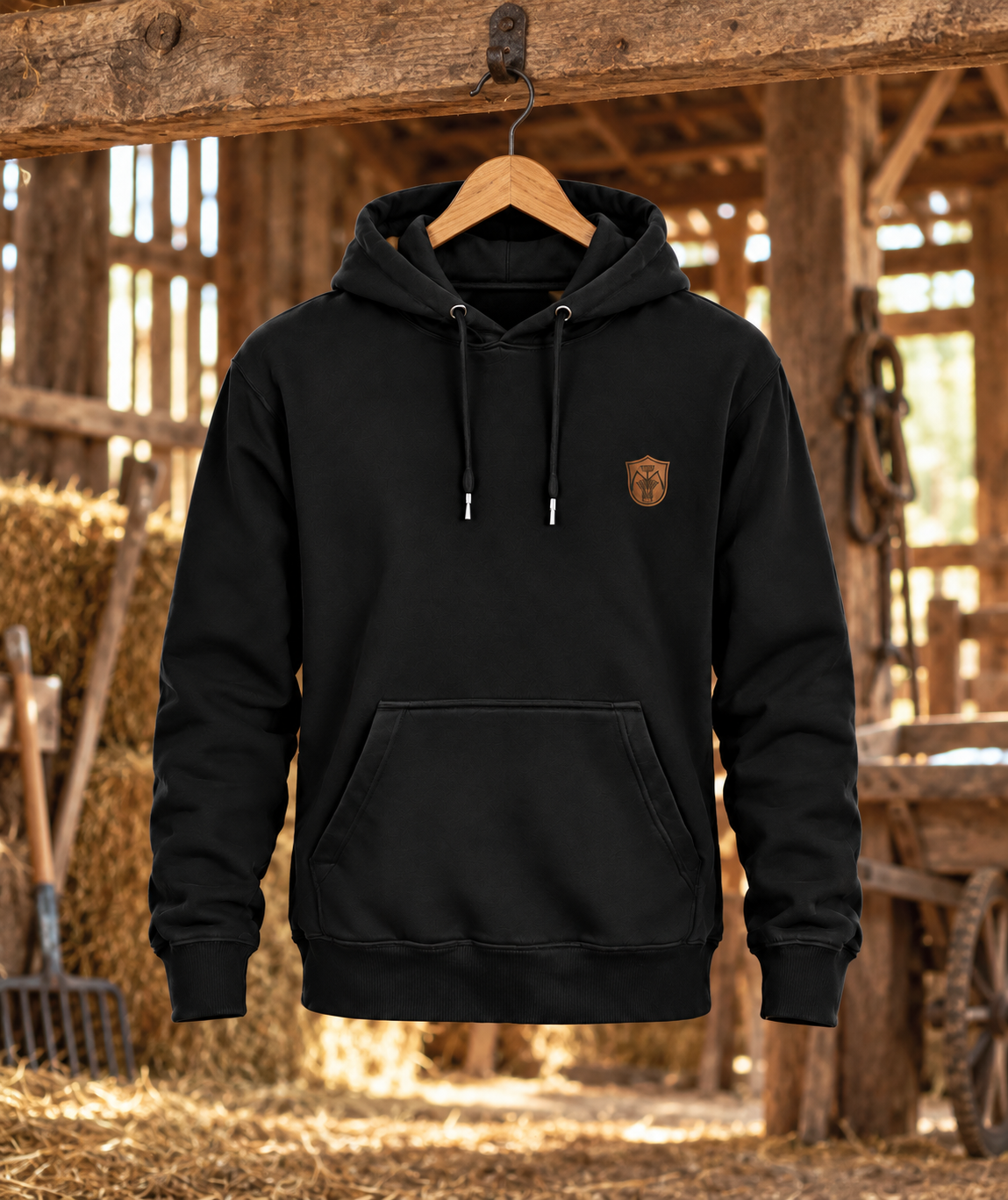 Schwarzer Landwirt Hoodie mit kleinem Brustwappen am Holzkleiderbügel in einer Scheune