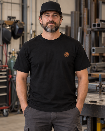 Erwachsener Mann trägt das schwarze Workaholicz Metallbauer T-Shirt ww28 mit kleinem Brustwappen in einer Metallwerkstatt