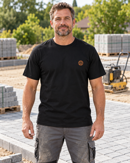 Erwachsener Mann trägt das schwarze Workaholicz Pflasterer T-Shirt ww30 mit kleinem Brustwappen auf einer Pflasterbaustelle