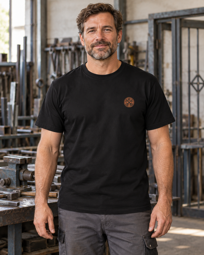 Erwachsener Mann trägt das schwarze Workaholicz Schlosser T-Shirt WW31 mit kleinem Zunftwappen in einer Schlosserei